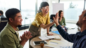 Team celebrating and high-fiving around table about webinar on Amplify, the online leadership training course for nonprofits from the Center for Creative Leadership